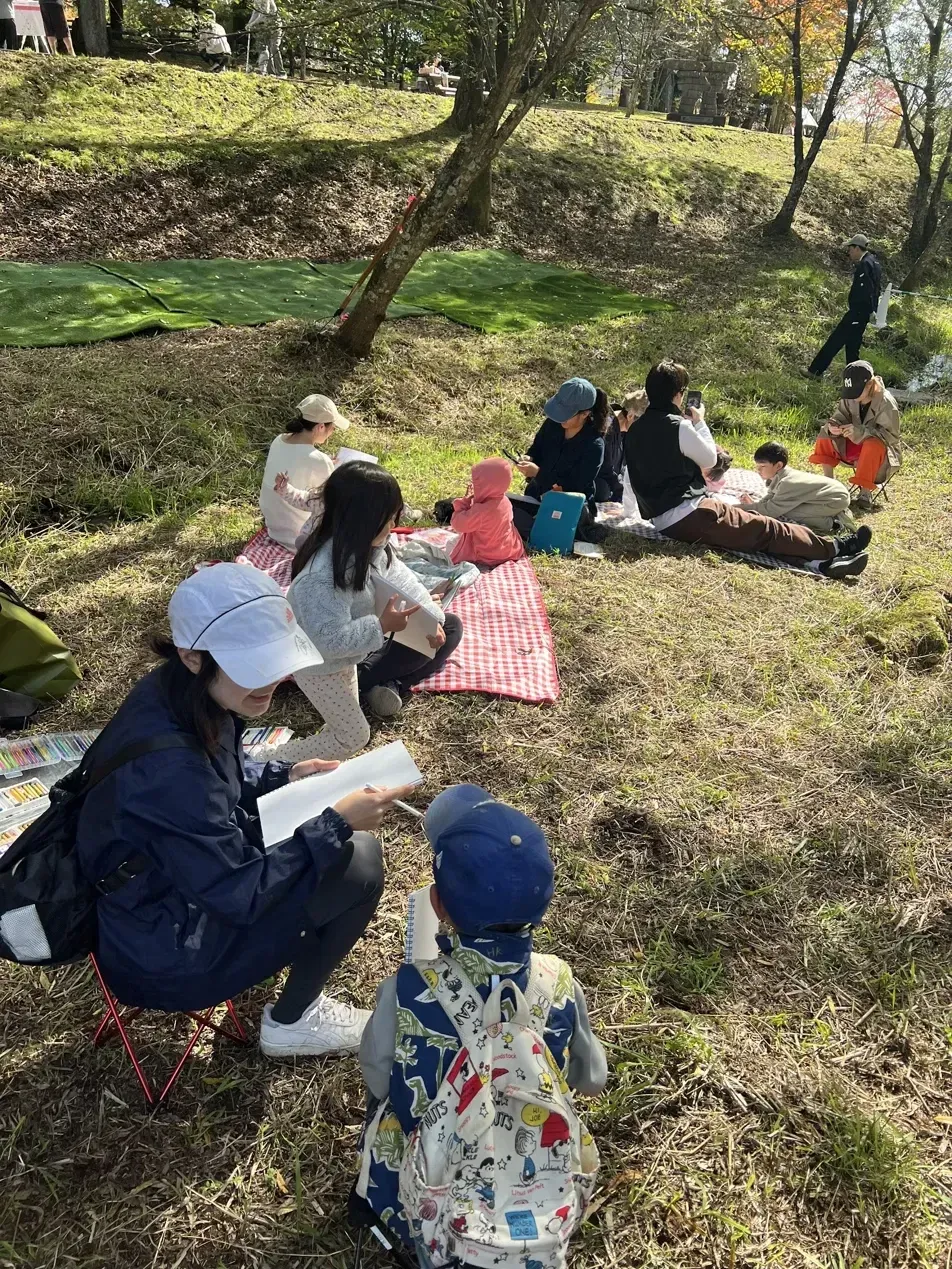 People sitting on picnic blankets and drawing beneath the trees at Yukawa no Hi.